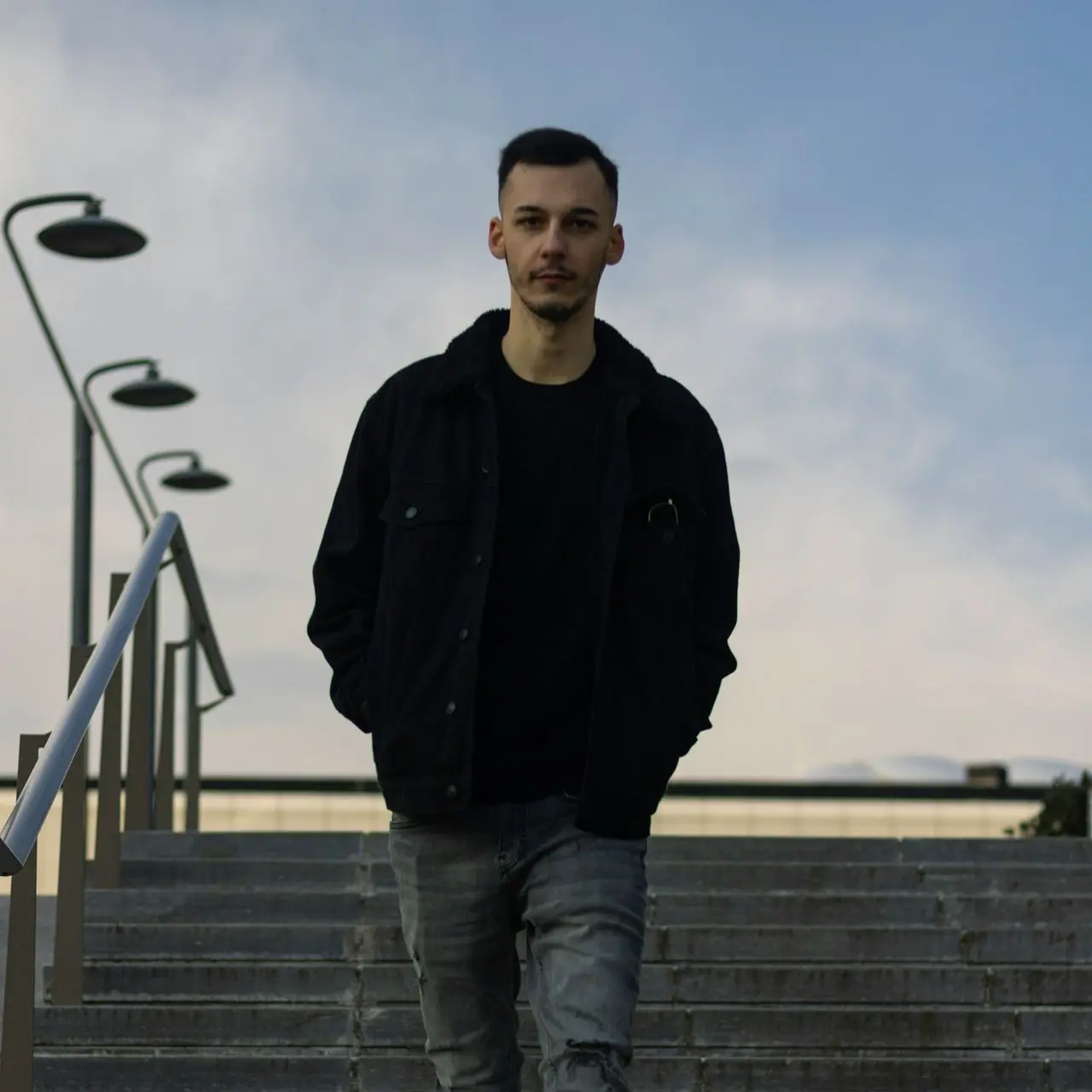 man in black jacket and blue denim jeans standing on stairs